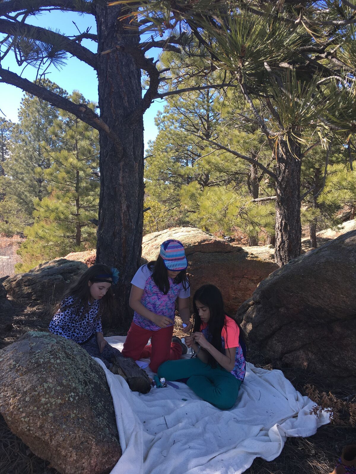 Three kids share a picnic blanket among granite boulders and ponderosa pines.