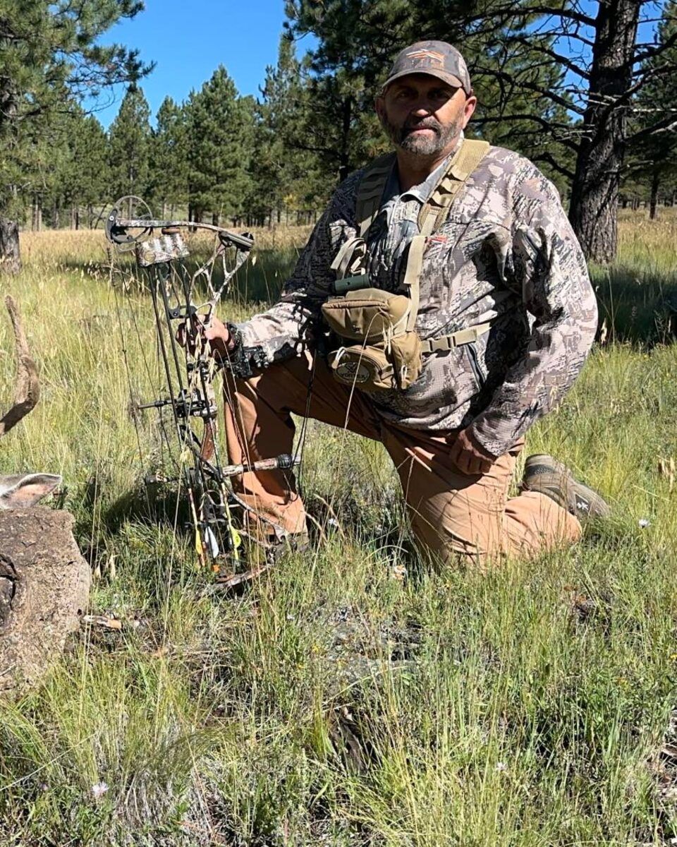 Yancey kneels in a ponderosa meadow with his compound bow.