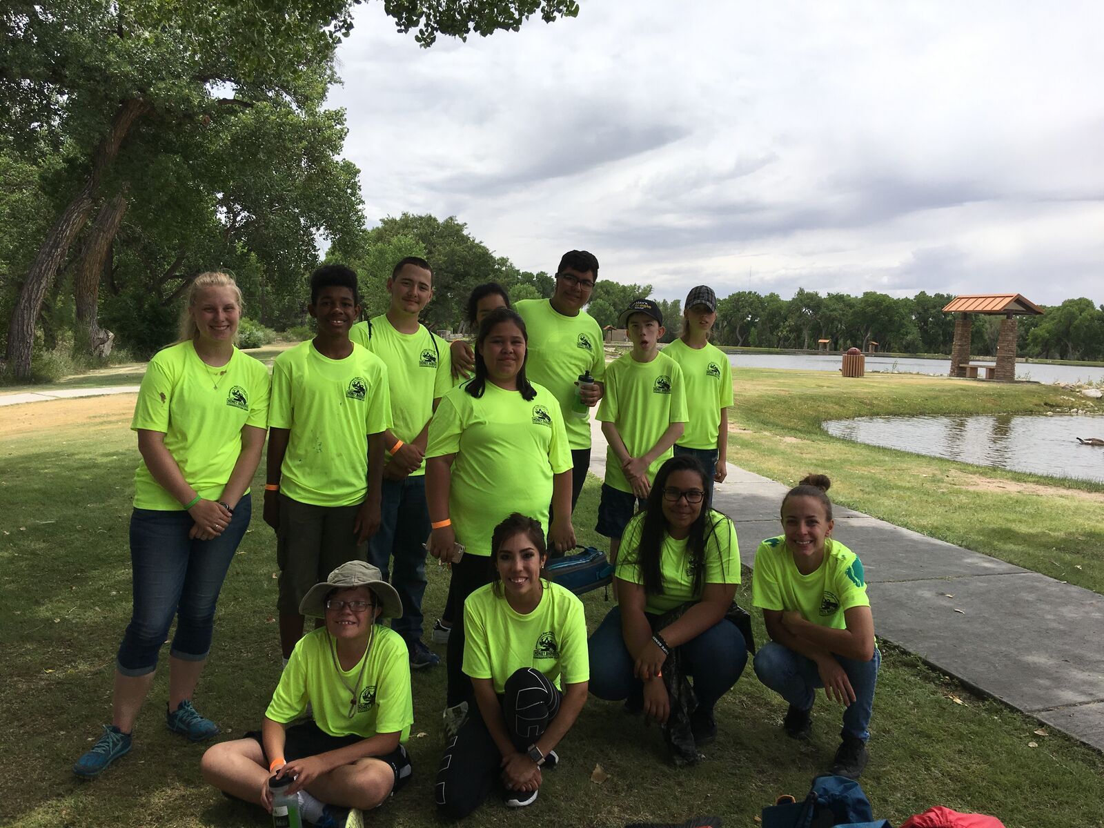 A group in yellow shirts gathered on the grass by the water.