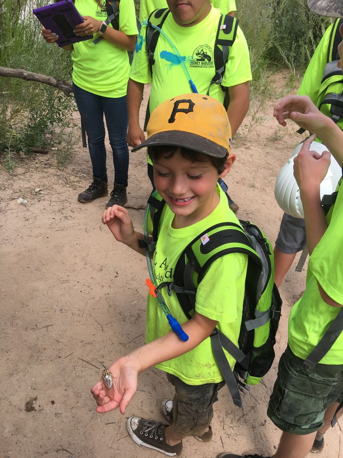 A boy in a cap looks closely at something tiny in his palm.