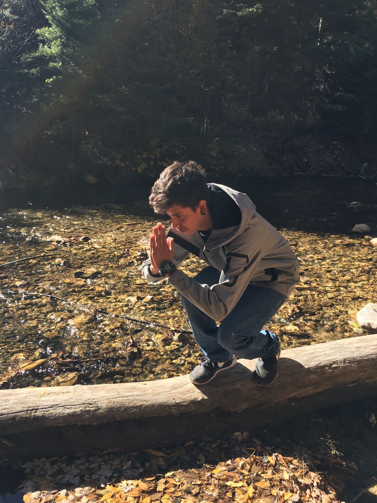 A boy crouches on a log over a creek bed covered in golden aspen leaves.