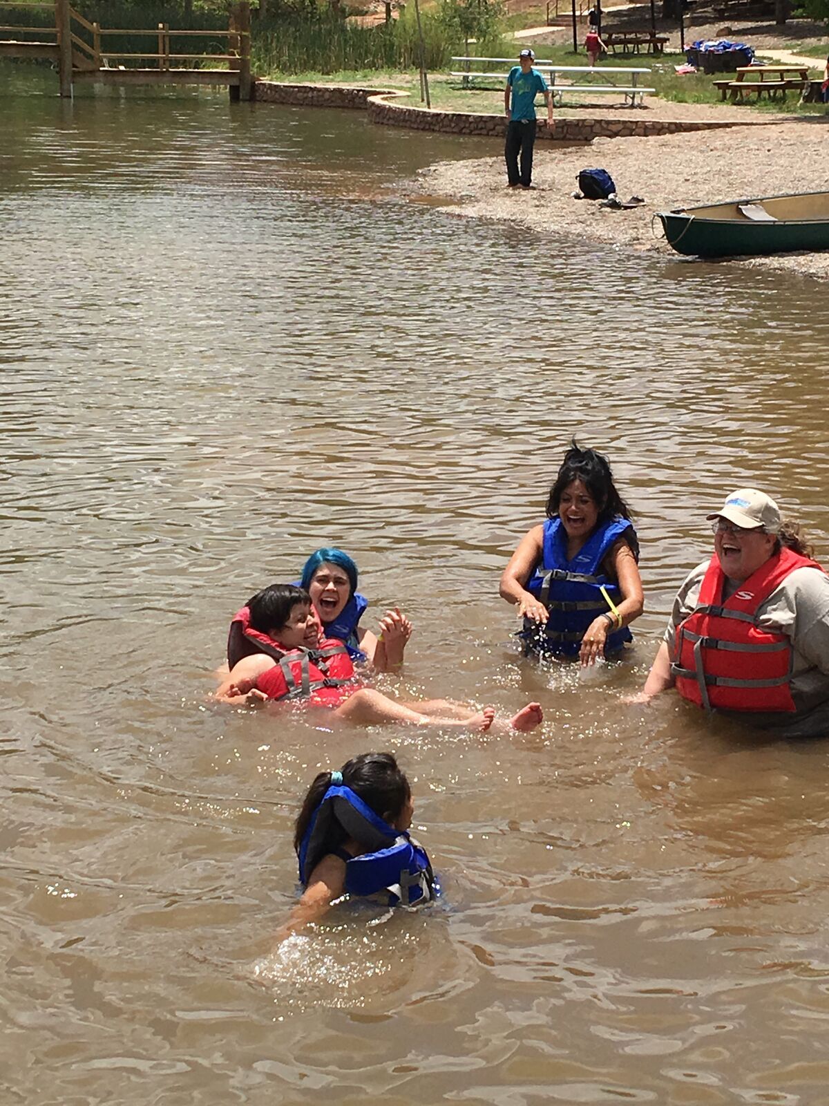 Kids and instructors in life jackets laugh and splash together in the lake at Glorieta.